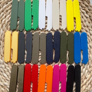 May include: A collection of colorful, rectangular, plastic items with a textured surface and a notched design. The items are arranged on a woven, circular surface. Colors include green, white, beige, yellow, black, blue, red, orange, and pink.