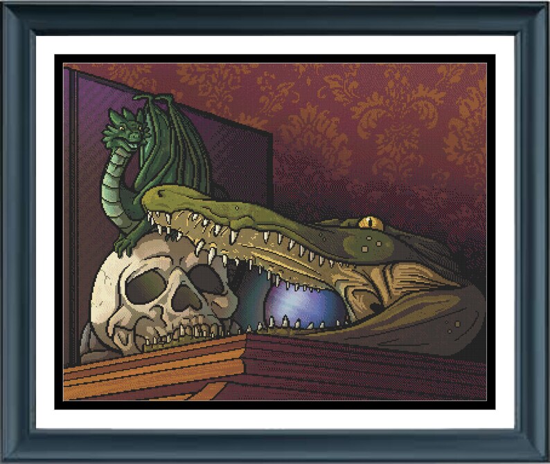May include: A framed cross-stitch artwork featuring a green dragon perched atop a human skull, positioned next to a large green alligator head with an open mouth containing a glowing purple orb, all set against a dark red damask patterned background.