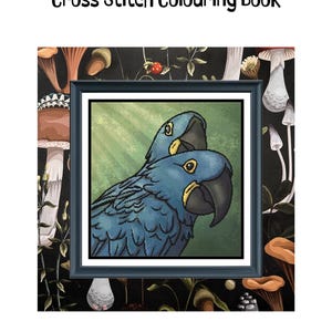 May include: A Hyacinth Macaws Cross Stitch Colouring Book featuring a framed cross-stitch pattern of two blue macaws with yellow eye rings and black beaks. The design measures 200 x 200 stitches, 11 x 11 inches at 14ct, and uses 75 colours.