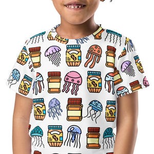 May include: A white t-shirt featuring a colorful pattern of cartoon jellyfish and jars. The design includes various colors like blue, pink, orange, and yellow. The shirt is short-sleeved and worn by a young child.
