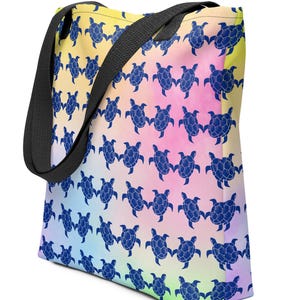 May include: A tote bag featuring a repeating pattern of dark blue sea turtles against a vibrant, multi-colored watercolor background that transitions from yellow to pink, blue, and green. The bag has two sturdy black fabric shoulder straps.