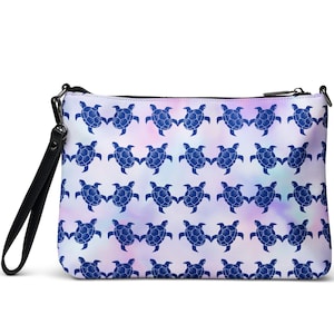 May include: A rectangular zippered pouch featuring a repeating pattern of dark blue sea turtles against a soft, pastel-colored watercolor background. The pouch includes a black wrist strap attached to the side with a silver-toned metal clasp.