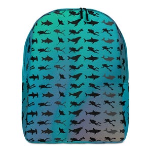 May include: A backpack featuring a gradient teal and blue background with a repeating pattern of black silhouettes depicting scuba divers, sharks, manta rays, and dolphins. The bag has a rounded top, a main zippered compartment, and black zippers.