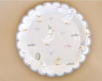 Puede incluir: Plato de papel blanco con borde festoneado, decorado con ilustraciones de patos, lazos y hierba. El plato tiene un borde azul claro y es adecuado para un baby shower o una fiesta infantil.