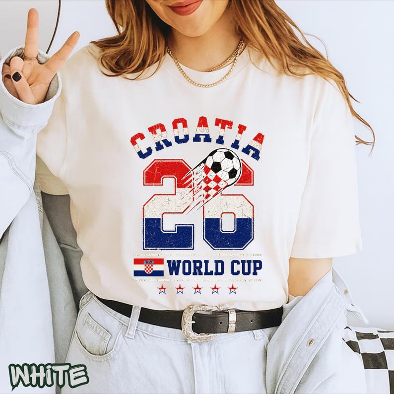 May include: A white short-sleeve t-shirt featuring a graphic with the text CROATIA 26 and WORLD CUP. The design includes a soccer ball, a checkered pattern, the Croatian flag, and five stars, all rendered in a distressed red, white, and blue color scheme.