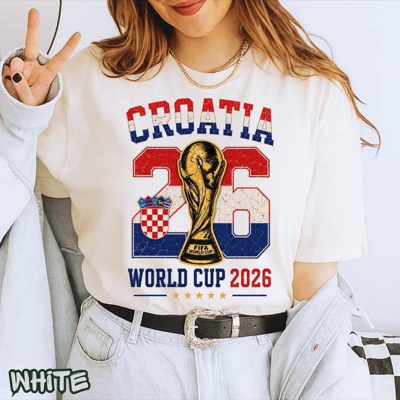 May include: A white t-shirt featuring a graphic with the text CROATIA, the number 26, and WORLD CUP 2026. The design includes a gold trophy illustration, the Croatian coat of arms, and a distressed red, white, and blue color scheme.