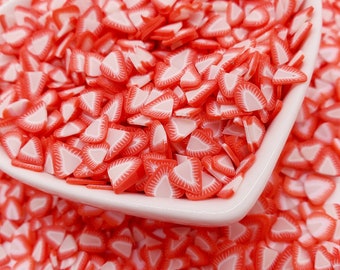 May include: A heart-shaped white dish filled with red and white strawberry-shaped polymer clay slices. The slices are scattered around the dish, creating a vibrant and colorful display. These decorative pieces are ideal for crafting and DIY projects.