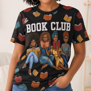 May include: Black t-shirt with the words "BOOK CLUB" in white block letters. The shirt features an illustration of four women reading books, with scattered book graphics. The person wearing the shirt is smiling.