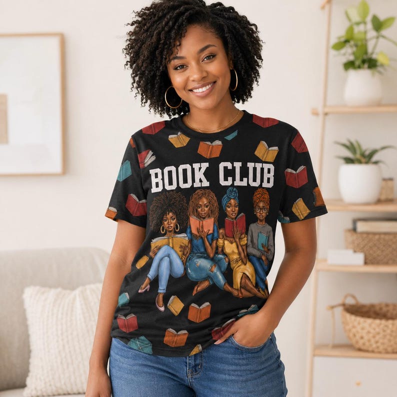 May include: Black t-shirt with the words "BOOK CLUB" in white block letters. The shirt features an illustration of four women reading books, with scattered book graphics. The person wearing the shirt is smiling.
