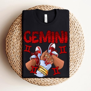 May include: Black t-shirt with the word "GEMINI" in red leopard print. The design includes red and white sneakers, hands with gold jewelry, and Gemini zodiac symbols.