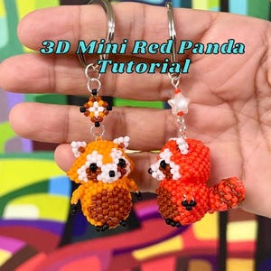 Op de afbeelding: Twee kralen sleutelhangers met rode panda's. De ene panda is oranje en bruin, de andere is rood en wit. De sleutelhangers hebben zilveren ringen en decoratieve kralenaccenten. De tekst "3D Mini Red Panda Tutorial" wordt boven de sleutelhangers weergegeven.