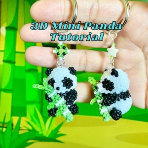 Könnte beinhalten: Zwei handgefertigte Schlüsselanhänger mit 3D-Pandabären. Die Pandas sind weiß mit schwarzen Akzenten und halten grünen Bambus. Die Schlüsselanhänger haben silberne Ringe und den Text "3D Mini Panda Tutorial".
