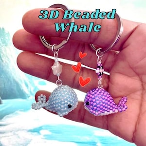 May include: Two beaded whale keychains. One is light blue with a star charm, the other is purple. The keychains are attached to silver rings. The text "3D Beaded Whale" is above the keychains.