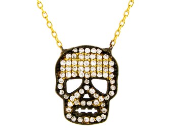 Puede incluir: Un collar de cadena dorada con un colgante de calavera negra incrustado con diamantes de imitación transparentes. El colgante tiene forma de calavera con un diseño detallado.