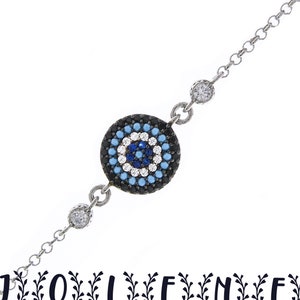 May include: Silver bracelet with a blue and white evil eye charm. The charm is surrounded by black stones.