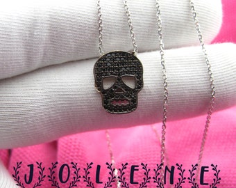 Puede incluir: Un collar de cadena de plata con un colgante de calavera de diamantes negros.