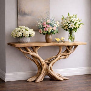 May include: A natural wood console table with a unique, branch-like base. The table supports three vases of flowers, including white lilies, pink and blue roses, and white hydrangeas. The table is made of light brown wood.