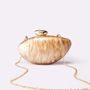 Può includere: Pochette ovale perlata con tracolla a catena dorata. La borsa presenta un effetto marmorizzato nei toni del crema e dell'oro, con una chiusura dorata sulla parte superiore. La catena è a maglie dorate delicate.