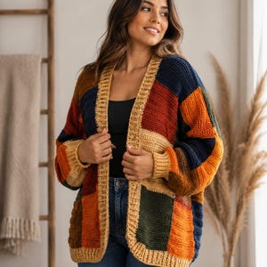 May include: A long-sleeved, open-front cardigan featuring a patchwork design of crocheted rectangular panels in navy blue, burnt orange, mustard yellow, and forest green. The garment has a ribbed mustard yellow trim along the front opening.