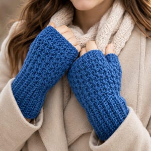 May include: A pair of vibrant blue fingerless gloves featuring a textured, raised stitch pattern on the main body and a ribbed cuff at the wrist. The gloves are worn with a beige coat and a matching beige knitted scarf around the neck.