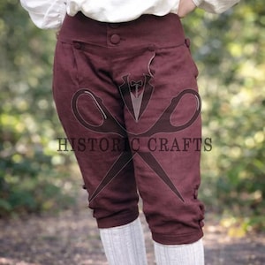 May include: Burgundy historical breeches with button details. The knee-length trousers feature a high waist and button closures. The text "HISTORIC CRAFTS" is visible on the garment. The breeches are paired with white socks.