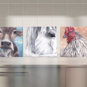 Puede incluir: Tres pinturas enmarcadas de animales de granja. La primera pintura es de una vaca marrón con un fondo de cielo azul. La segunda pintura es de la cabeza de un caballo blanco. La tercera pintura es de un gallo blanco con una cresta y barbillas rojas.