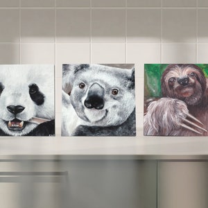 May include: Three framed paintings of animals. The first painting features a black and white panda bear with a bamboo stick in its mouth. The second painting features a gray koala bear. The third painting features a brown sloth with green foliage in the background.