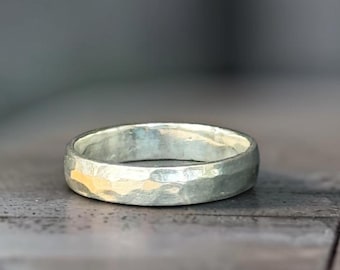 May include: A silver ring with a hammered texture. The ring is round and has a slightly uneven surface, reflecting light. The ring is set against a blurred, neutral background. Jewelry.
