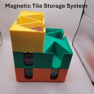 May include: A Magnetic Tile Storage System featuring stacked, multi-coloured plastic bins in yellow, green, and orange. The structure has open-top compartments and U-shaped cutouts on the sides, revealing stacks of colourful magnetic tiles inside.