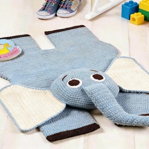 May include: A light blue crocheted elephant-shaped rug with a matching head and trunk, and two white and blue wings. The rug is surrounded by children's toys, including a book, building blocks, and sneakers.