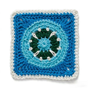 May include: A square, crocheted item featuring a circular design in shades of blue, green, and white. The center is a lighter blue, surrounded by a dark green circle, and then a light blue ring. The outer edge is a darker blue with a white border.