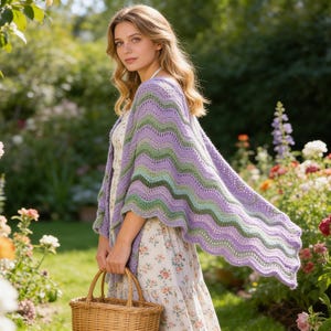 May include: A woman wearing a lavender, green, and dark green crocheted shawl with a wavy pattern. She is holding a wicker basket and standing in a garden filled with colorful flowers.