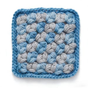 Puede incluir: Posavasos cuadrado de ganchillo en tonos azules y grises. El posavasos presenta un patrón texturizado con un borde azul liso. El artículo hecho a mano se utiliza probablemente para proteger las superficies de bebidas frías o calientes.