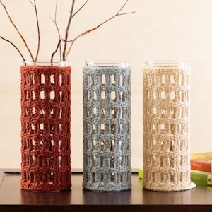 May include: A white ceramic mug with a black handle and the text "But First, Coffee" in a bold, black font. The mug is set against a blurred background, suggesting a cozy setting.