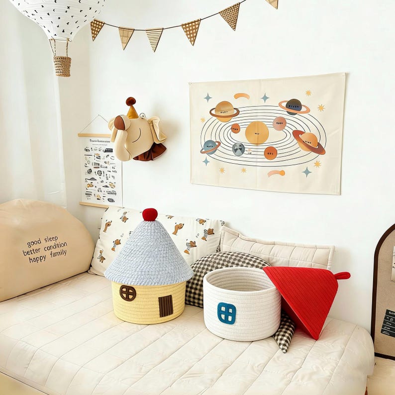 May include: A child's bedroom scene with a house-shaped basket, a white rope basket with a blue window, and a red triangle-shaped pillow. A tapestry of planets hangs on the wall, and a hot air balloon decorates the ceiling.