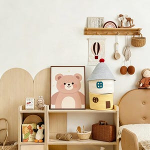 May include: A children's room scene with a framed bear illustration, a house-shaped storage basket, and a wooden shelf with decorative items. The color palette includes soft pinks, yellows, and natural wood tones, creating a cozy atmosphere.