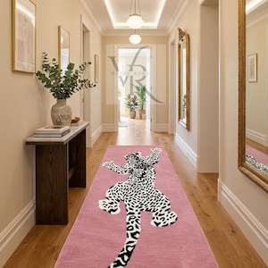 Può includere: Un tappeto rosa per corridoio con un motivo leopardato in bianco e nero. Il tappeto rettangolare è posizionato in un corridoio con pavimento in legno. Il design del leopardo è centrato, con la coda rivolta verso il basso.