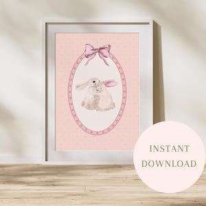 Könnte beinhalten: Ein gerahmter Druck mit einer Aquarellillustration von zwei umarmenden Hasen in einem ovalen Rahmen, gekrönt von einer rosa Schleife. Der Hintergrund ist ein hellrosa gepunktetes Muster. Die Worte "SOFORT-DOWNLOAD" stehen auf einem rosa Kreis.