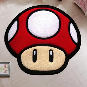 May include: A red, white, and black mushroom-shaped rug. The rug has a large white circle on top, white spots, and a beige base with two black oval eyes. This rug is a fun, decorative item for a child's room or games room.