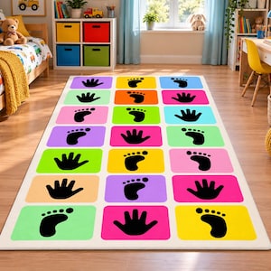 May include: A rectangular area rug featuring a grid of colourful rectangles in shades of pink, yellow, green, orange, blue, and purple. Each rectangle contains a black silhouette of either a human handprint or a footprint pattern for play.