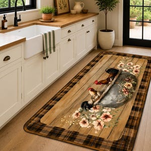 May include: A rectangular kitchen floor mat featuring a rustic wood plank pattern, a dark brown and black plaid border, and a central graphic of two roosters standing near a metal basin adorned with clusters of pink and white floral blossoms.