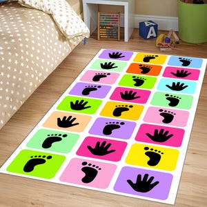 May include: A rectangular floor mat featuring a grid of colourful rounded rectangles in shades of purple, green, orange, pink, blue, and yellow. Each rectangle contains a black silhouette of either a human handprint or a human footprint.