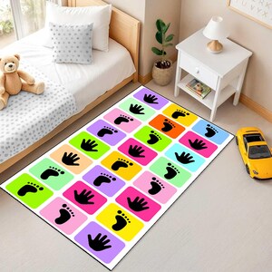 May include: A rectangular area rug featuring a grid of colourful squares in shades of pink, yellow, green, orange, blue, and purple. Each square contains a black silhouette of either a human handprint or a footprint arranged in a repeating pattern.