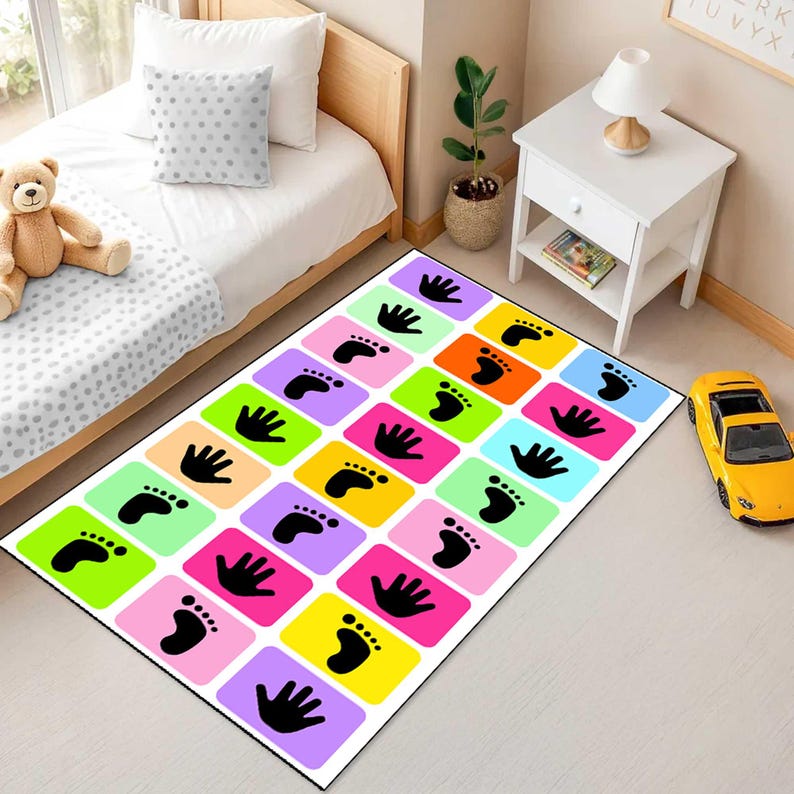 May include: A rectangular area rug featuring a grid of colourful squares in shades of pink, yellow, green, orange, blue, and purple. Each square contains a black silhouette of either a human handprint or a footprint arranged in a repeating pattern.