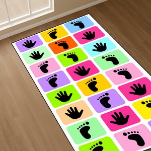 May include: A rectangular floor mat featuring a grid of colourful squares in shades of blue, yellow, orange, pink, green, and purple. Each square contains a black silhouette of either a human hand or a human foot, arranged in a repeating pattern.