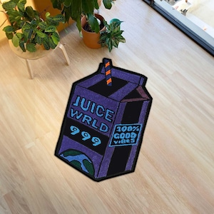 以下が含まれることがあります： JUICE WRLD、999、100% GOOD VIBESという青い文字が書かれた紫色のジュースパック型ラグ。上部にはオレンジと黒のストライプ柄のストロー、下部の隅には青と緑の地球儀のグラフィックがデザインされています。