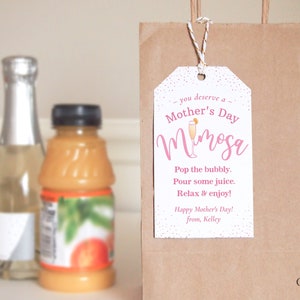 Pu&ograve; includere: Un'etichetta regalo bianca con testo rosa che dice "ti meriti un Mimosa della Festa della Mamma". L'etichetta include anche una piccola illustrazione di una bevanda mimosa e il testo "Stappa le bollicine. Versa un po' di succo. Rilassati e goditi! Buona Festa della Mamma! da Kelley".