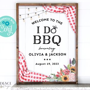 May include: A white sign with a wooden frame, announcing a "I Do BBQ" party honoring Olivia & Jackson on August 19, 2023. The sign features a red and white checkered tablecloth, string lights, and watercolor flowers.