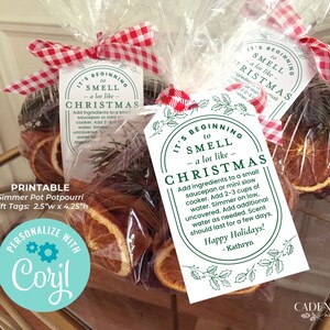 May include: Printable gift tags for simmer pot potpourri. The tags are white with green holly leaves and the text "It's beginning to smell like Christmas". The text includes instructions for making the potpourri. The tags are tied with a red and white gingham ribbon to a clear bag filled with dried orange slices and sprigs of greenery.