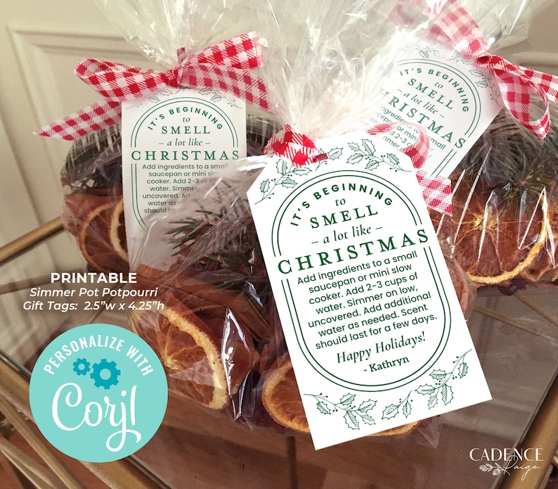 May include: Printable gift tags for simmer pot potpourri. The tags are white with green holly leaves and the text "It's beginning to smell like Christmas". The text includes instructions for making the potpourri. The tags are tied with a red and white gingham ribbon to a clear bag filled with dried orange slices and sprigs of greenery.